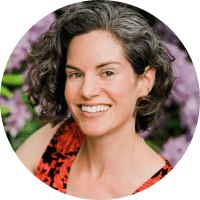 Portrait of a smiling woman with short curly hair, wearing a red and black top, set against a background of purple flowers.