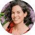 Portrait of a smiling woman with short curly hair, wearing a red and black top, set against a background of purple flowers.