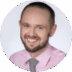 Portrait of a smiling man with a beard, wearing a light pink shirt, possibly celebrating his first-time college enrollment, against a light green background.