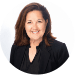 Professional headshot of a smiling woman with shoulder-length brown hair, wearing a black blazer and a black blouse, set against a light green background.