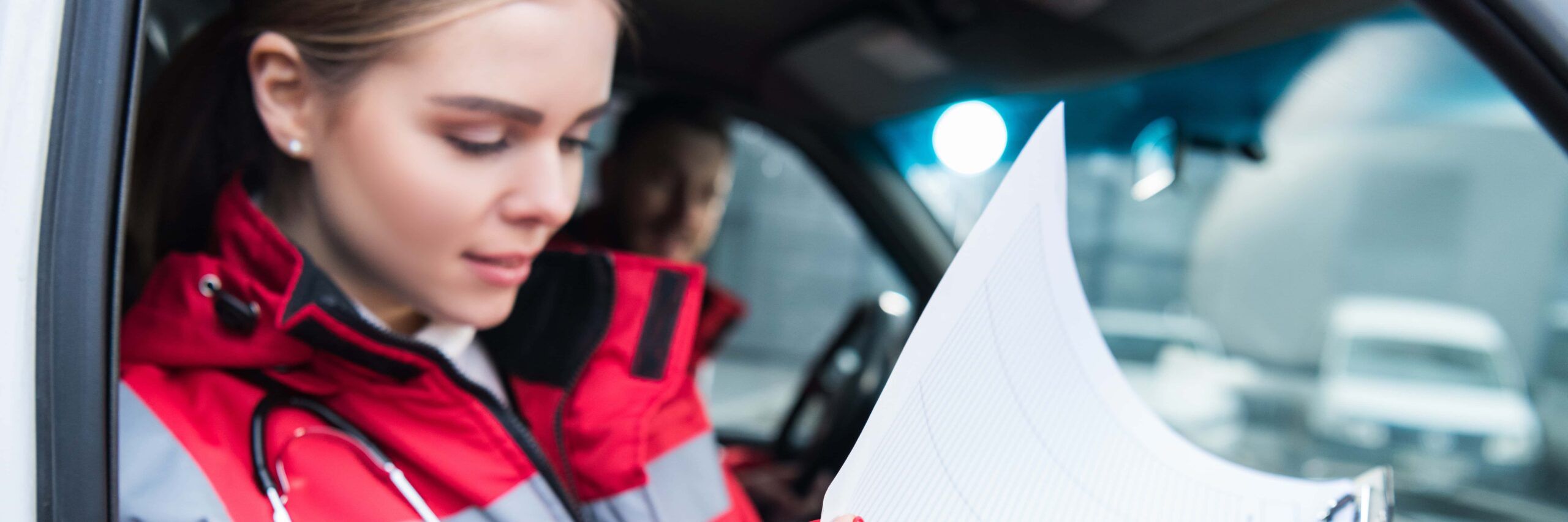 A focused emergency medical technician reviewing medical paperwork inside an ambulance.