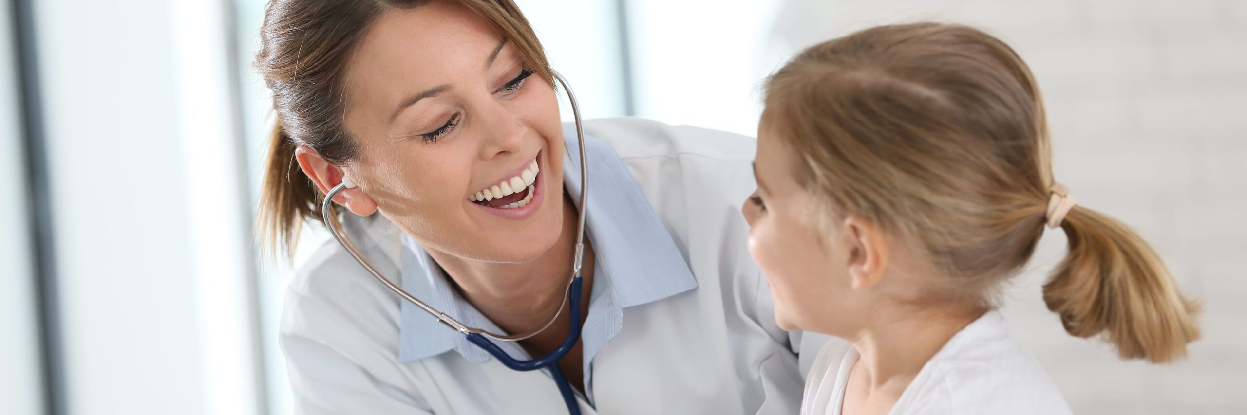 A female doctor with a stethoscope smiling at a young girl, creating a comforting atmosphere during a psychiatric care consultation in a bright, modern clinic.