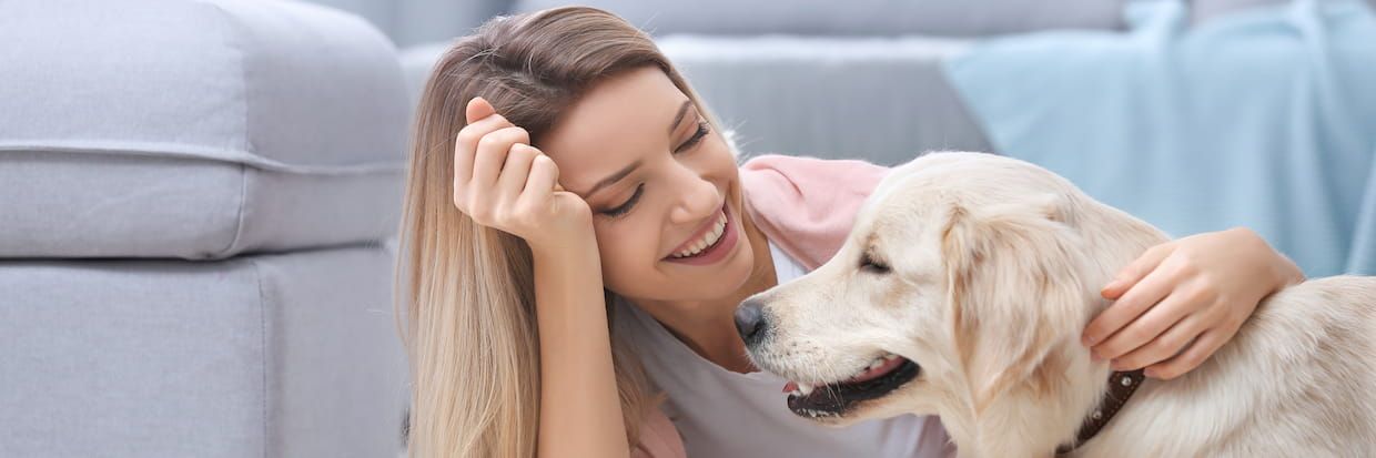 A joyful young woman lounging on the floor next to a couch, smiling and petting a golden retriever while studying for her veterinary technician exam, creating a comforting and friendly atmosphere.