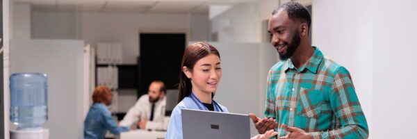 A male office worker and a female colleague discussing over a laptop in an inclusive, bright office space, with other coworkers in the background.