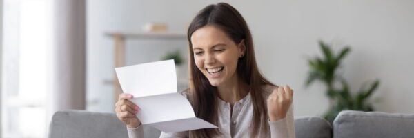 A joyful woman reads a letter while sitting on a couch, expressing excitement with a clenched fist and a wide smile, embodying a moment of positive psychiatric mental health.