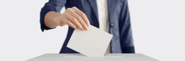 A college student in a business suit casting a vote by placing a ballot into a voting box on a table, with a white background.