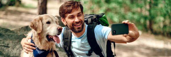 A joyful man with a beard taking a selfie with his golden retriever dog in a forested area, both appearing happy, showcasing a day in the life typical of those pursuing animal careers.