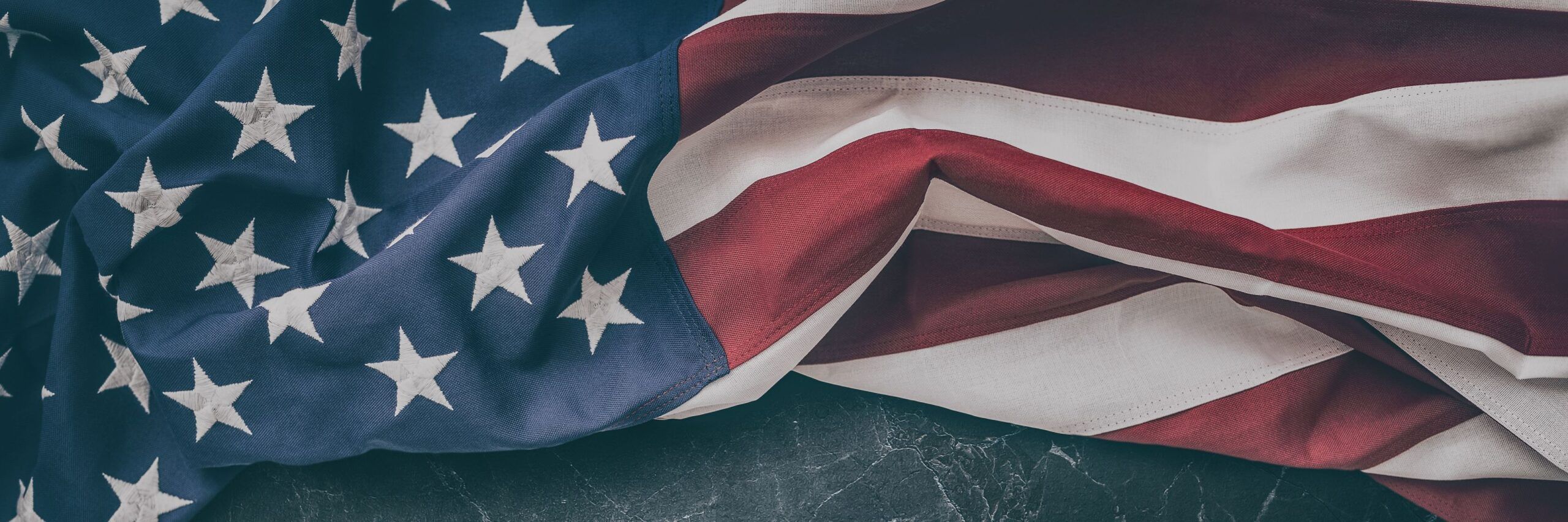 Close-up of an american flag neatly arranged, showing the stars and stripes in rich colors against a dark textured background.