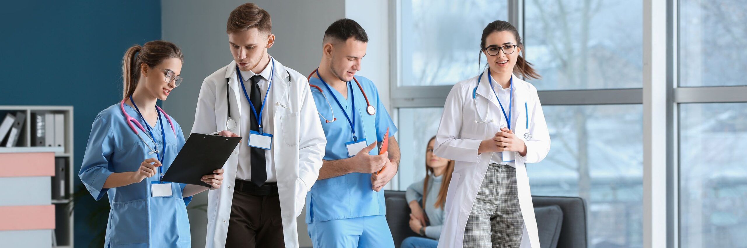 A group of medical staff, including two men and two women in lab coats and scrubs, engaged in conversation while walking through a hospital corridor.