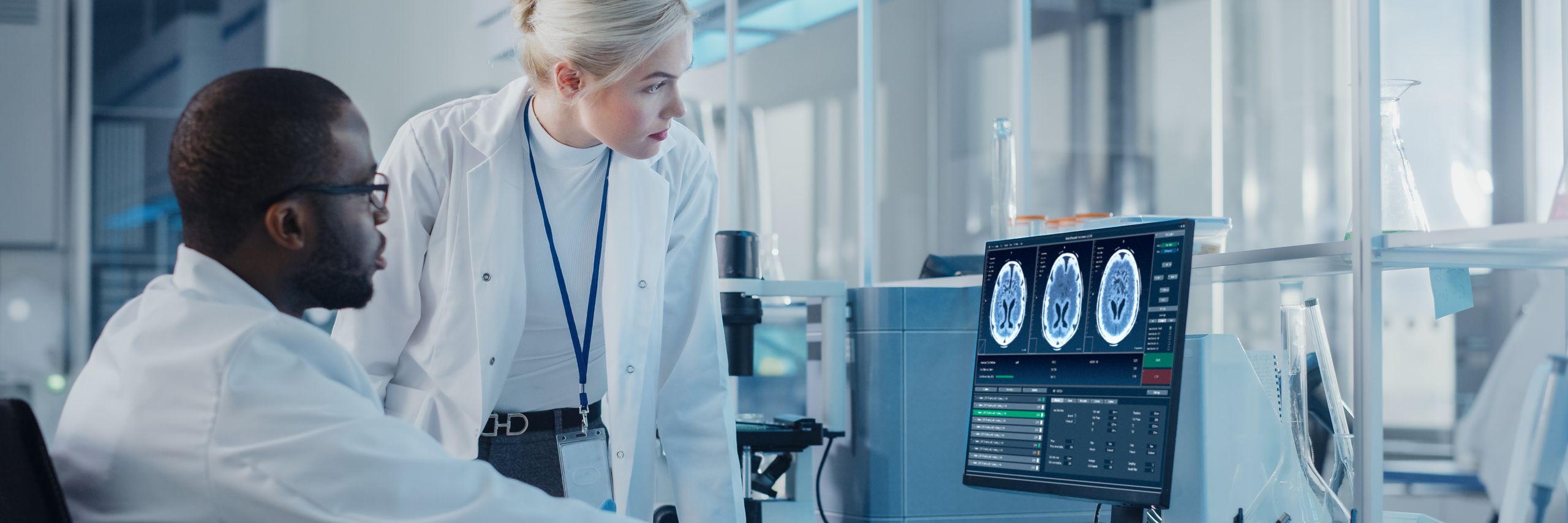 Two scientists, a man and a woman, analyze brain scan images on a monitor in a high-tech laboratory setting.