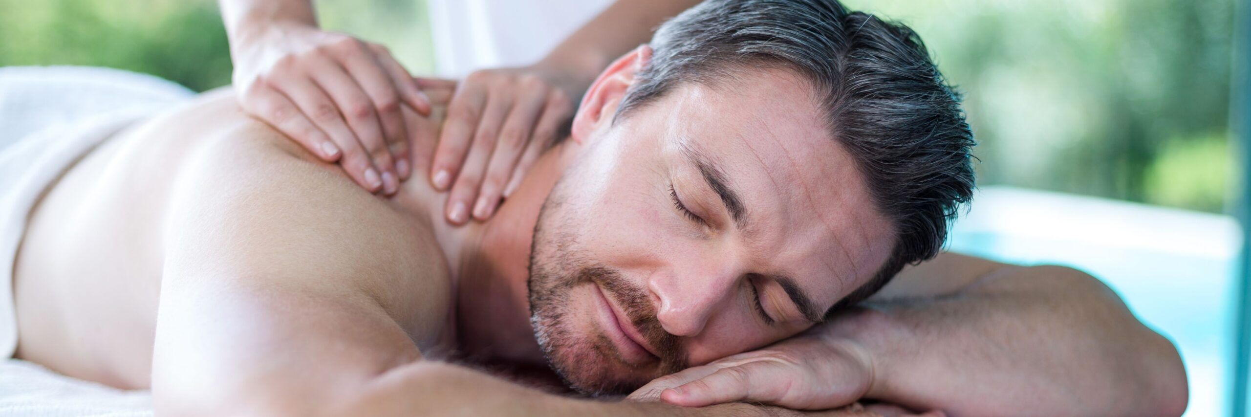 A relaxed man receiving a professional back massage at a spa during his massage therapy class, with a serene expression and eyes closed.