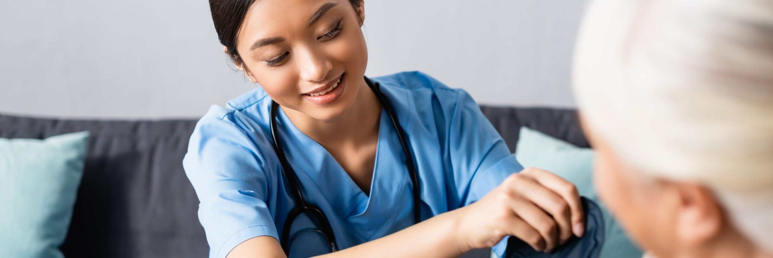 A compassionate nurse in blue scrubs gently holds the arm of an elderly patient, engaging warmly during an academic support session in home healthcare.