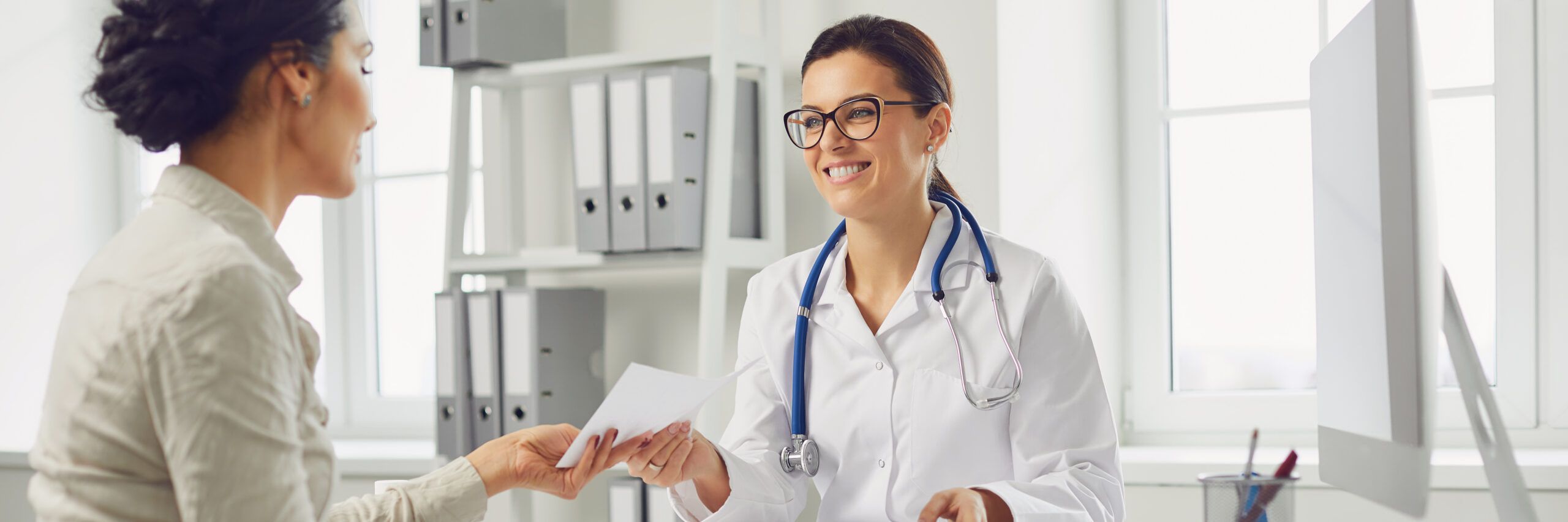 Smiling female patient at consultation with woman doctor sitting at table in office clinic.