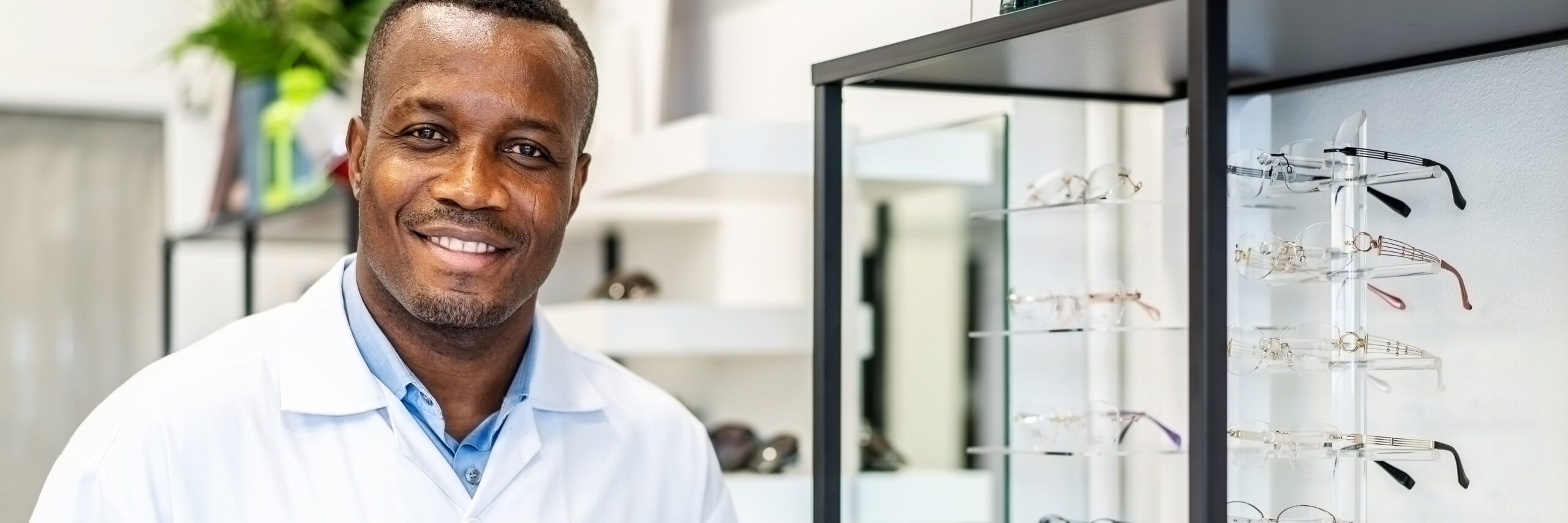 Eyesight And Vision Concept. View of smiling african american attractive optician working with tablet in his glasses shop.