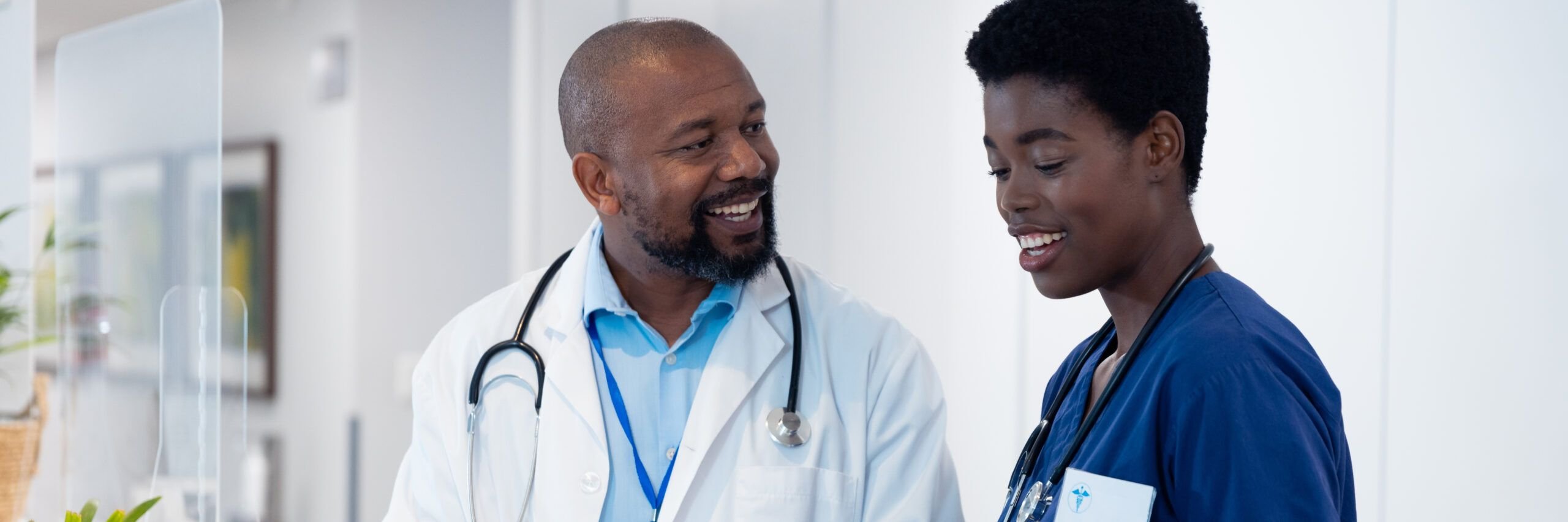 Smiling african american male and female doctor with tablet talking in hospital corridor. Hospital, medical and healthcare services.