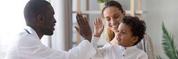 A joyful family scene with a black man giving a high-five to a young boy, while a smiling caucasian woman looks on, all standing in a bright, domestic setting.