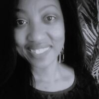 Black and white close-up photo of a woman smiling softly at the camera, with long dark hair and geometric earrings. Leafy patterned background partially visible on the right.