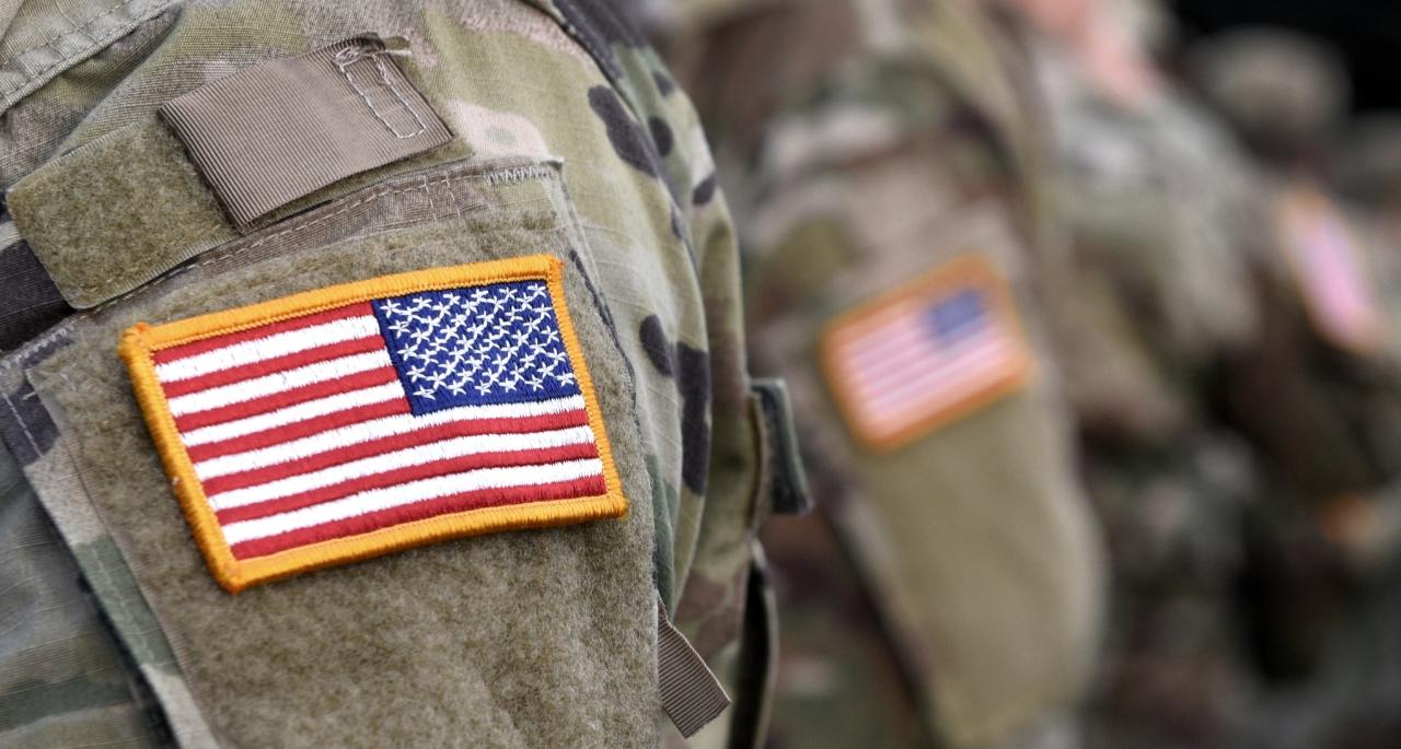 Close-up of uniformed soldiers wearing camouflage, with a prominent U.S. flag patch on the shoulder of the nearest veteran; other veterans with similar patches are visible in the background, as highlighted in our Online Guide.